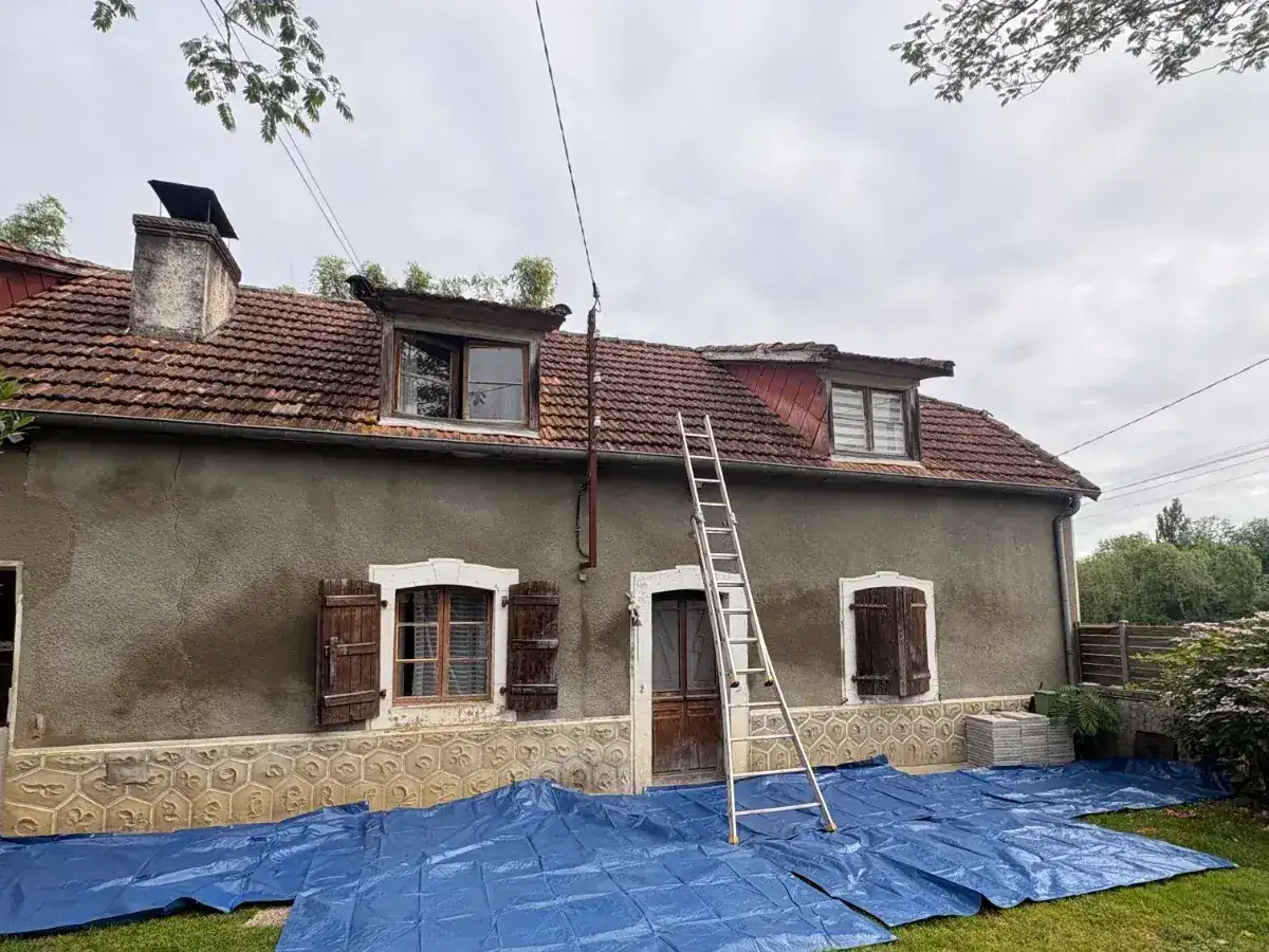 Maison béarnaise en galets et chaux dont la toiture ancienne est fatiguée, échelle appuyée et bâche au sol